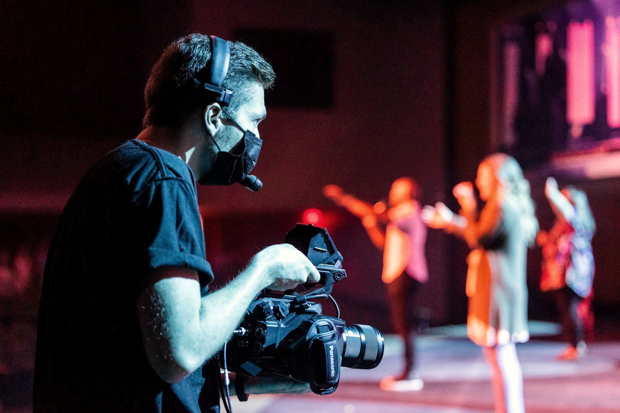 Camera operator filming a live stage performance under coloured lights